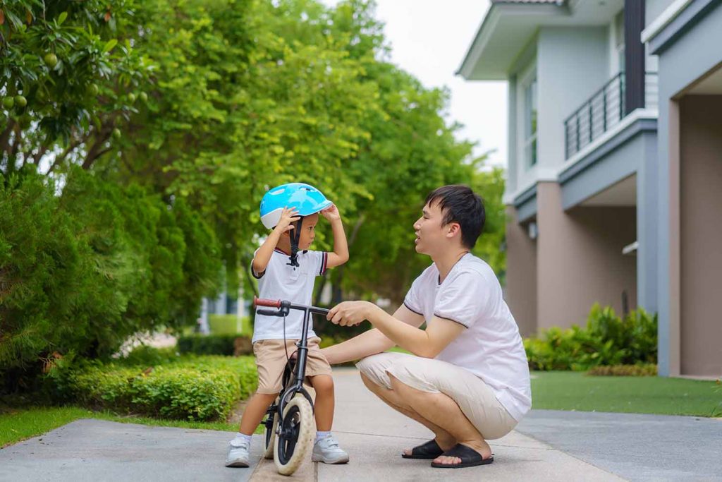 Asian father wears a helmet for his son while teaching his child
